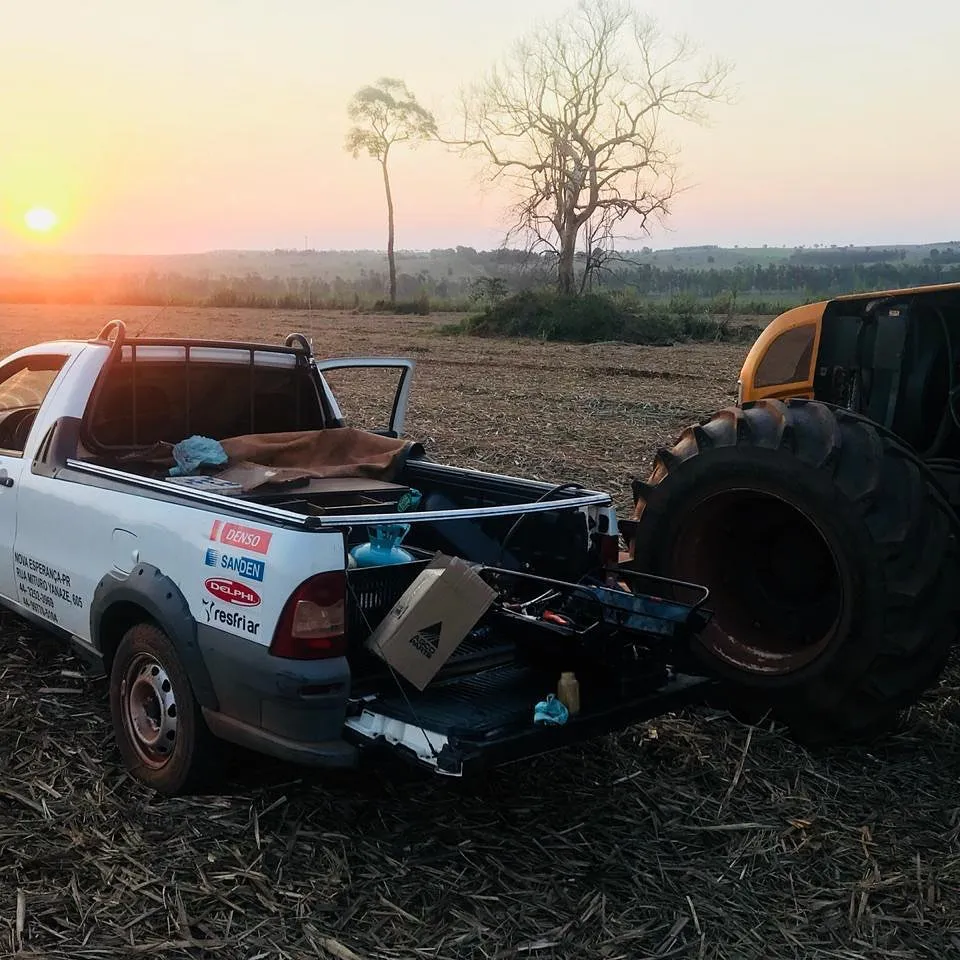 Picape de atendimento ao lado de máquina agrícola em lavoura ao pôr do sol