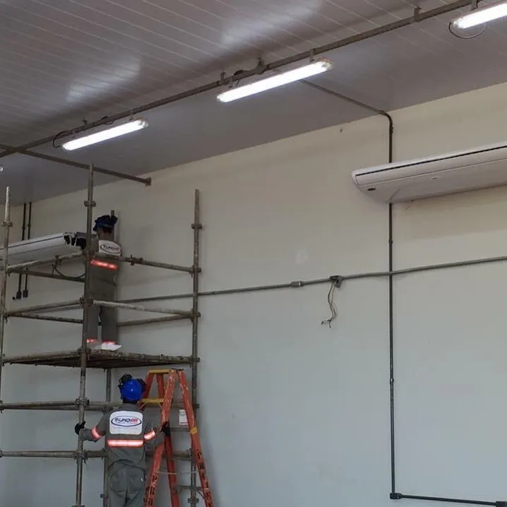 Técnicos com EPI instalando ar-condicionado em galpão usando andaime