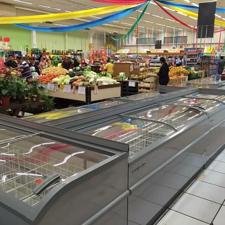 Ilhas de congelados em supermercado decorado, com setor de hortifrúti ao fundo