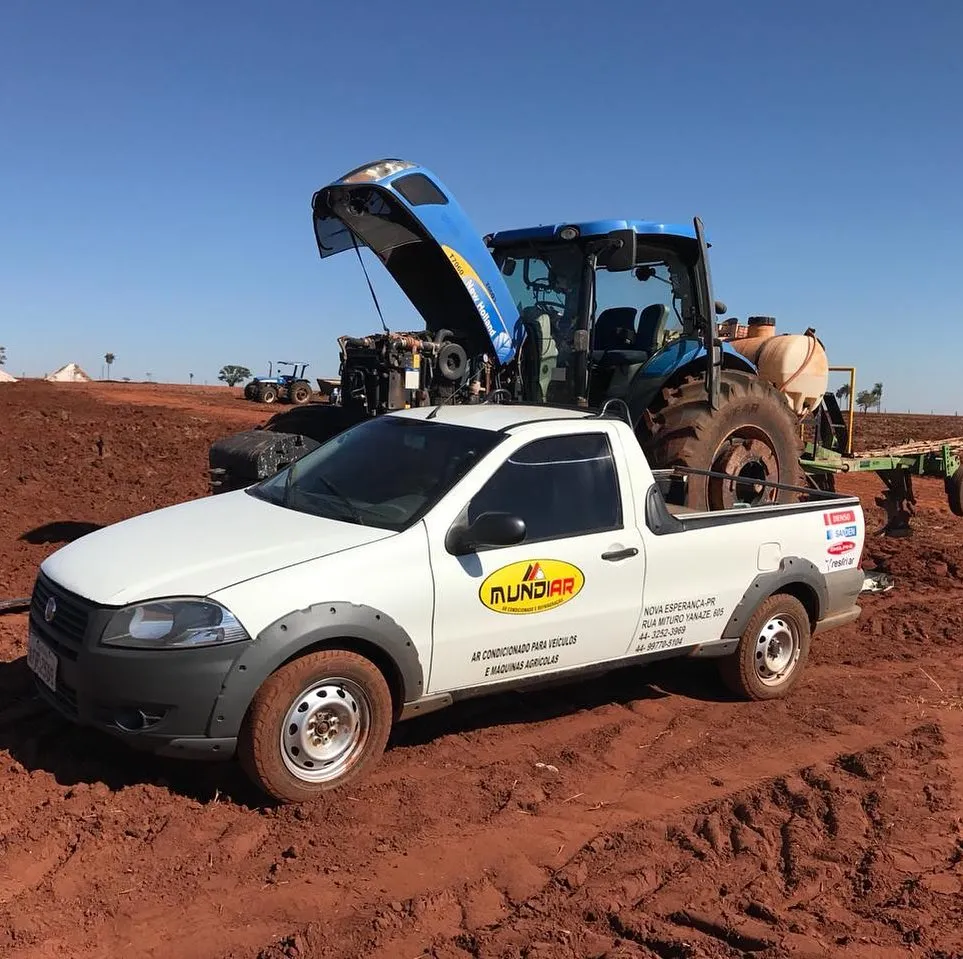 Picape Mundiar ao lado de trator New Holland com capô aberto em terra vermelha