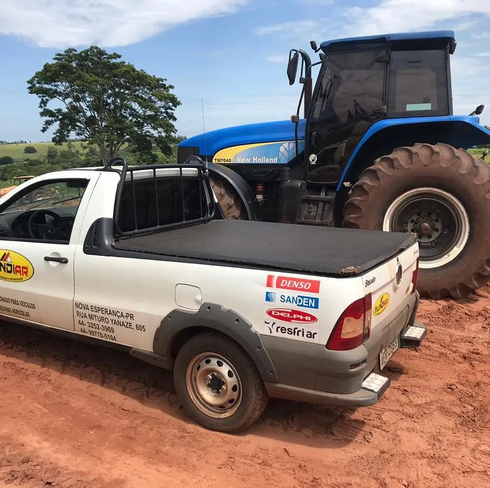 Trator New Holland TM7040 ao lado de picape de atendimento técnico no campo